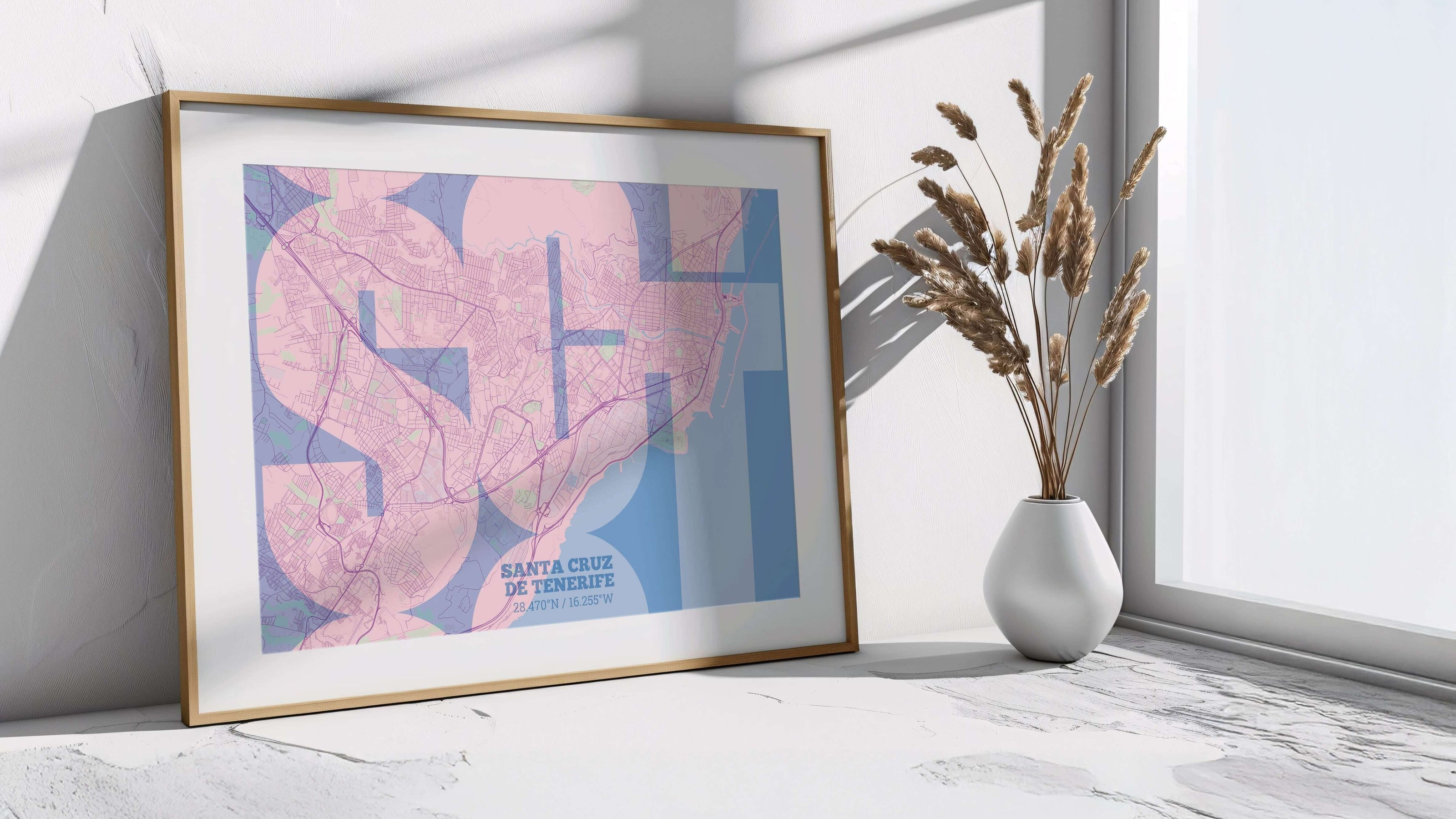 A cyan and pink map os SantaCruz de Tenerife on a mounted natural wood frame  leaning against a wall and a white floor