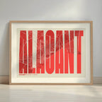Framed Alacant in Extra Compressed design, where the letters are tightly squeezed to fit the city's map shape designed in red and an off-white background with a white margin border in a warm lit minimalist setting