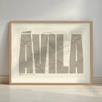 Framed Avila in Extra Compressed design, where the letters are tightly squeezed to fit the city's map shape designed in light brown and an off-white background with a white margin border in a warm lit minimalist setting