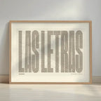 Framed Barrio de Las Letras in Extra Compressed design, where the letters are tightly squeezed to fit the city's map shape designed in light brown and an off-white background with a white margin border in a warm lit minimalist setting