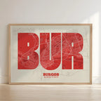 Framed Burgos in Super Bold design, a typographic poster where the city map is overlaid with extra-thick lettering for a modern, high-impact look designed in red and an off-white background with no border edge-to-edge print leaning against a wall