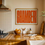 Modern interior design with a Chamberi in Extra Compressed design, where the letters are tightly squeezed to fit the city's map shape designed in orange and an off-white background, displayed on a living room wall