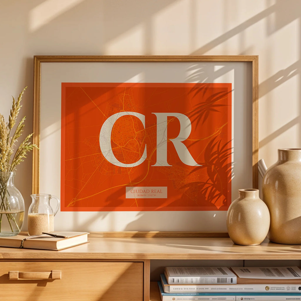 Diseño de interiores moderno con la lámina de Ciudad Real en el diseño la Clásica, inspirado en la tipografía cincelada con una fuente elegante que crea un bonito contraste visual diseñado en naranja y fondo blanco roto, expuesto en la pared de un salón
