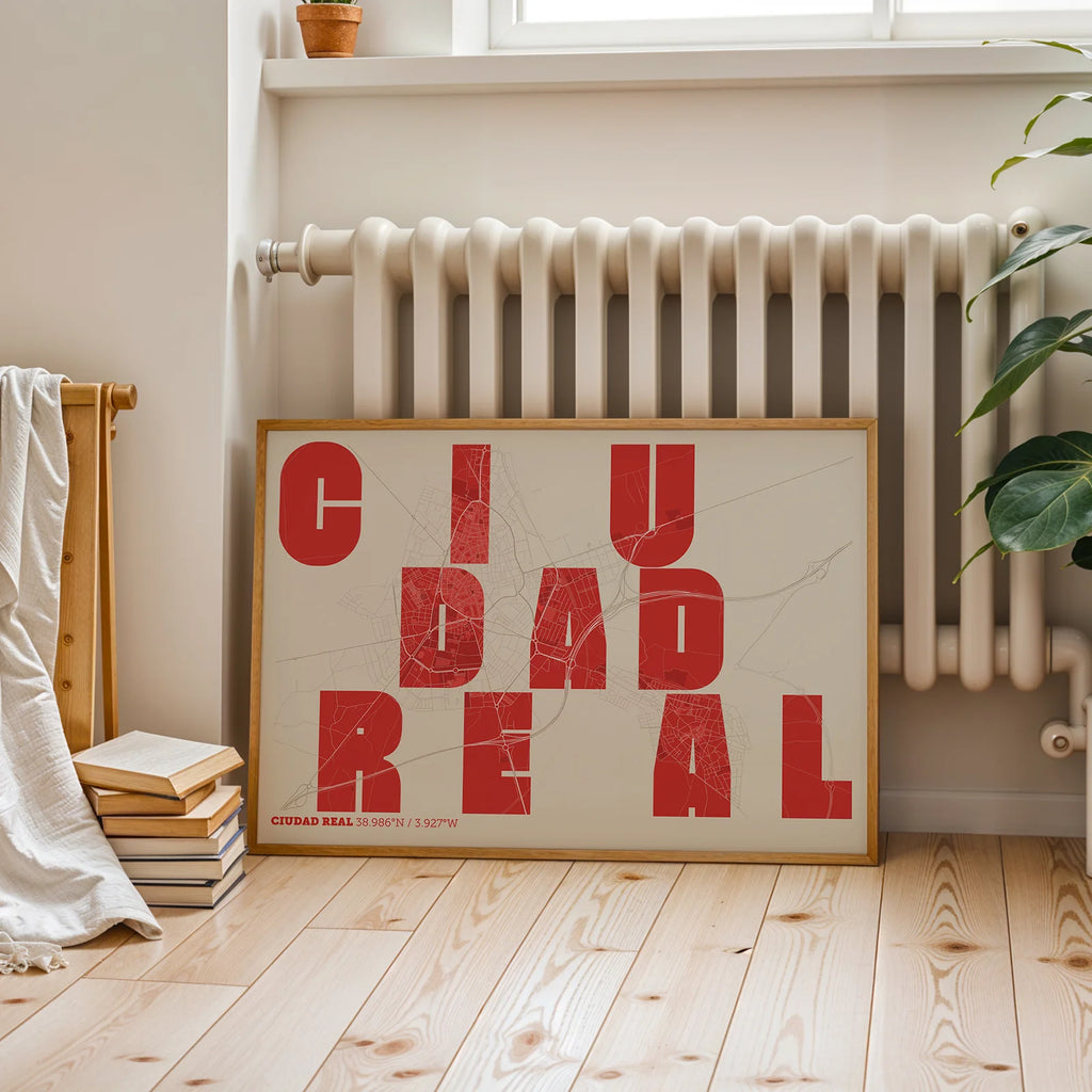 Diseño de interiores moderno con la lámina de Ciudad Real en el diseño la Revoltosa, donde las letras del nombre aparecen aleatoriamente en diferentes líneas para un diseño urbano realmente original diseñado en rojo y fondo blanco roto, expuesto en la pared de un salón