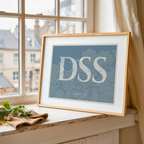 Diseño de interiores moderno con la lámina de Donostia en el diseño la Clásica, inspirado en la tipografía cincelada con una fuente elegante que crea un bonito contraste visual diseñado en gris azulado y fondo blanco roto, expuesto en la pared de un salón