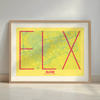 Framed Elche in Ultralight design, a minimalist aesthetic combining urban cartography with modern, extra-thin elegant lettering designed in yellow and fuchsia with a white margin border in a warm lit minimalist setting