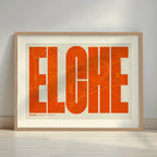 Framed Elche in Extra Compressed design, where the letters are tightly squeezed to fit the city's map shape designed in orange and an off-white background with a white margin border in a warm lit minimalist setting
