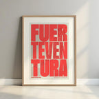 Framed Fuerteventura in Extra Compressed design, where the letters are tightly squeezed to fit the city's map shape designed in red and an off-white background with a white margin border in a warm lit minimalist setting