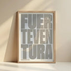 Framed Fuerteventura in Extra Compressed design, where the letters are tightly squeezed to fit the city's map shape designed in light brown and an off-white background with no border edge-to-edge print leaning against a wall