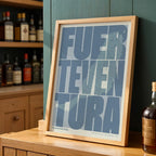 Modern interior design with a Fuerteventura in Extra Compressed design, where the letters are tightly squeezed to fit the city's map shape designed in bluish gray and an off-white background, displayed on a living room wall