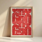 Framed Girona in Inseparable design, featuring the city's abbreviation in expressive typography over a detailed urban map designed in red and an off-white background with no border edge-to-edge print leaning against a wall
