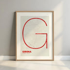 Framed Girona in Ultralight design, a minimalist aesthetic combining urban cartography with modern, extra-thin elegant lettering designed in red and an off-white background with a white margin border in a warm lit minimalist setting