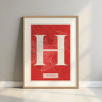 Framed Huesca in Classic design, inspired by chiseled typography with an elegant font that creates a beautiful visual contrast designed in red and an off-white background with a white margin border in a warm lit minimalist setting