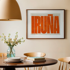 Modern interior design with a Iruña in Extra Compressed design, where the letters are tightly squeezed to fit the city's map shape designed in orange and an off-white background, displayed on a living room wall