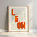 Framed Leon in Unruled design, where the city name letters appear randomly across different lines for a truly original urban layout designed in orange and an off-white background with a white margin border in a warm lit minimalist setting
