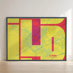 Framed Lleida in Inseparable design, featuring the city's abbreviation in expressive typography over a detailed urban map designed in yellow and fuchsia with no border edge-to-edge print leaning against a wall