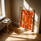 Diseño de interiores moderno con la lámina de Lugo en mi diseño la Inseparable, una visión artística con una tipografía expresiva que muestra la abreviatura del nombre sobre el mapa detallado diseñado en naranja y fondo blanco roto, expuesto en la pared de un salón