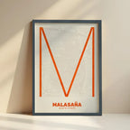 Framed Malasaña, Madrid, in Ultralight design, a minimalist aesthetic combining urban cartography with modern, extra-thin elegant lettering designed in orange and an off-white background with no border edge-to-edge print leaning against a wall