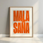 Framed Malasaña, Madrid, in Extra Compressed design, where the letters are tightly squeezed to fit the city's map shape designed in orange and an off-white background with a white margin border in a warm lit minimalist setting
