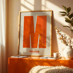 Diseño de interiores moderno con la lámina de Melilla en mi diseño la Súper Bold, un póster tipográfico donde el mapa de la ciudad se fusiona con una tipografía extra gruesa para un impacto visual moderno diseñado en naranja y fondo blanco roto, expuesto en la pared de un salón