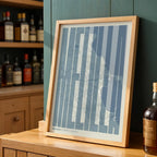 Diseño de interiores moderno con la lámina de Melilla en el diseño la Extra Comprimida, donde las letras se ajustan al ancho del mapa de la ciudad diseñado en gris azulado y fondo blanco roto, expuesto en la pared de un salón