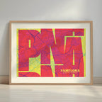 Framed Pamplona in Inseparable design, featuring the city's abbreviation in expressive typography over a detailed urban map designed in yellow and fuchsia with a white margin border in a warm lit minimalist setting