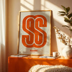 Modern interior design with a San Sebastian de los Reyes in Super Bold design, a typographic poster where the city map is overlaid with extra-thick lettering for a modern, high-impact look designed in orange and an off-white background, displayed on a living room wall