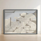 Framed San Sebastian in Inseparable design, featuring the city's abbreviation in expressive typography over a detailed urban map designed in light brown and an off-white background with no border edge-to-edge print leaning against a wall