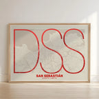 Framed San Sebastian in Ultralight design, a minimalist aesthetic combining urban cartography with modern, extra-thin elegant lettering designed in red and an off-white background with no border edge-to-edge print leaning against a wall