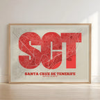 Framed Santa Cruz de Tenerife in Super Bold design, a typographic poster where the city map is overlaid with extra-thick lettering for a modern, high-impact look designed in red and an off-white background with no border edge-to-edge print leaning against a wall