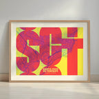 Framed Santa Cruz de Tenerife in Inseparable design, featuring the city's abbreviation in expressive typography over a detailed urban map designed in yellow and fuchsia with a white margin border in a warm lit minimalist setting