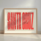Framed Santa Cruz de Tenerife in Extra Compressed design, where the letters are tightly squeezed to fit the city's map shape designed in red and an off-white background with a white margin border in a warm lit minimalist setting