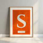Framed Santiago de Compostela in Classic design, inspired by chiseled typography with an elegant font that creates a beautiful visual contrast designed in orange and an off-white background with a white margin border in a warm lit minimalist setting