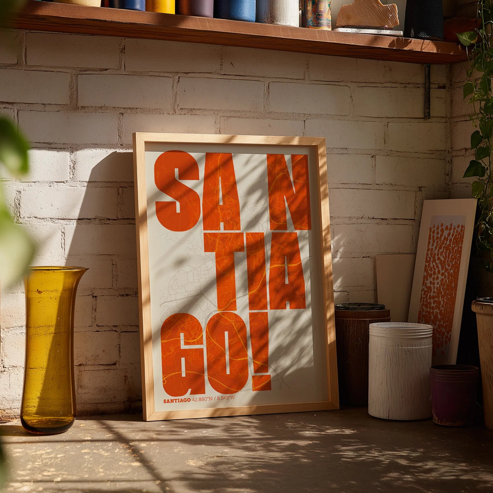 Diseño de interiores moderno con la lámina de Santiago de Compostela en el diseño la Revoltosa, donde las letras del nombre aparecen aleatoriamente en diferentes líneas para un diseño urbano realmente original diseñado en naranja y fondo blanco roto, expuesto en la pared de un salón