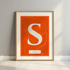 Framed Soria in Classic design, inspired by chiseled typography with an elegant font that creates a beautiful visual contrast designed in orange and an off-white background with a white margin border in a warm lit minimalist setting
