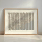 Framed Tarragona in Extra Compressed design, where the letters are tightly squeezed to fit the city's map shape designed in light brown and an off-white background with a white margin border in a warm lit minimalist setting