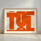 Framed Toledo in Inseparable design, featuring the city's abbreviation in expressive typography over a detailed urban map designed in orange and an off-white background with a white margin border in a warm lit minimalist setting