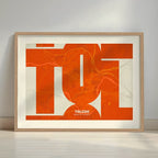 Framed Toledo in Inseparable design, featuring the city's abbreviation in expressive typography over a detailed urban map designed in orange and an off-white background with a white margin border in a warm lit minimalist setting