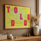 Diseño de interiores moderno con la lámina de Toledo en el diseño la Revoltosa, donde las letras del nombre aparecen aleatoriamente en diferentes líneas para un diseño urbano realmente original diseñado en amarillo y fucsia, expuesto en la pared de un salón