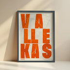 Framed Vallecas in Unruled design, where the city name letters appear randomly across different lines for a truly original urban layout designed in orange and an off-white background with no border edge-to-edge print leaning against a wall