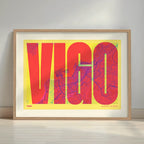 Framed Vigo in Extra Compressed design, where the letters are tightly squeezed to fit the city's map shape designed in yellow and fuchsia with a white margin border in a warm lit minimalist setting