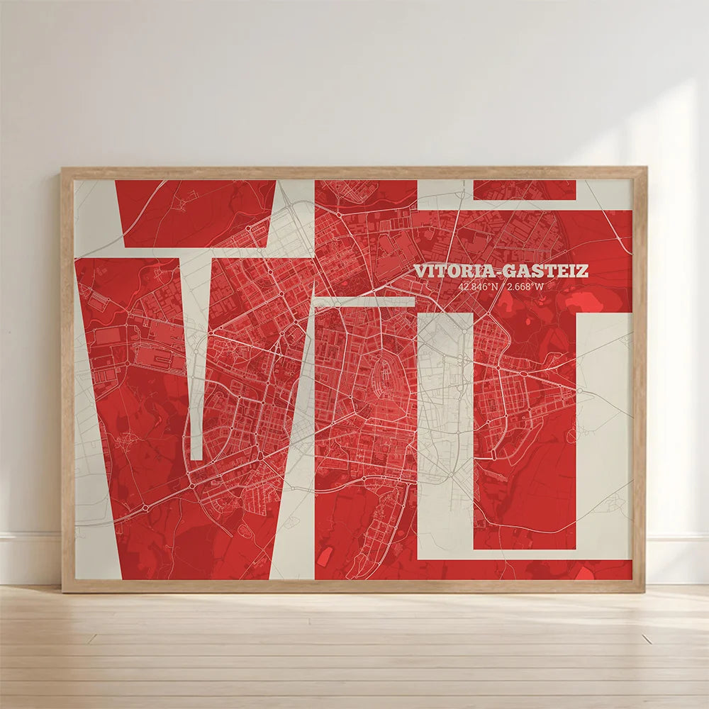 Framed Vitoria-Gasteiz in Inseparable design, featuring the city's abbreviation in expressive typography over a detailed urban map designed in red and an off-white background with no border edge-to-edge print leaning against a wall
